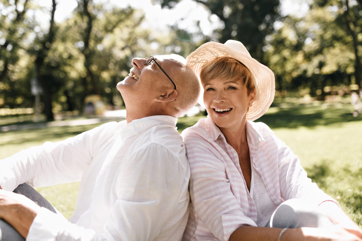 trendy short haired lady light hat striped blouse smiling sitting grass with old man glasses white shirt outdoor 1 - testamente - Familiehandlen